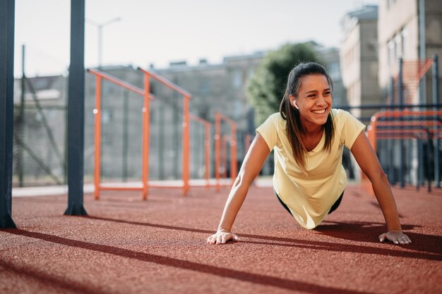 Smiling female doing push ups at sports ground