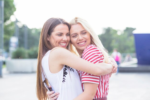 Smiling female friend hugging each other at outdoors