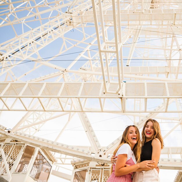 Smiling female friend standing under the white ferris wheel