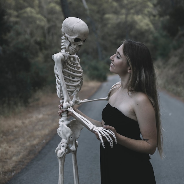 Femmina sorridente che tiene scheletro artificiale dell'uomo che sta sulla strada
