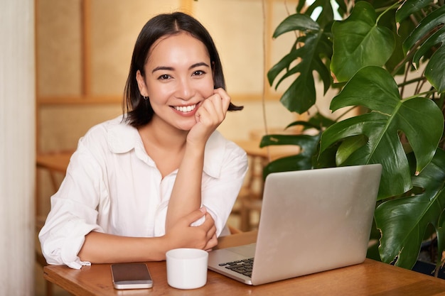 Smiling female manager freelancer or student sitting with laptop in cafe and working typing on compu