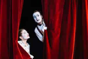 Free photo smiling female mime artist looking at male mime artist peeking from curtain