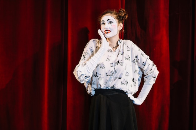 빨간 커튼 공상 앞에 서있는 웃는 여성 마임 아티스트