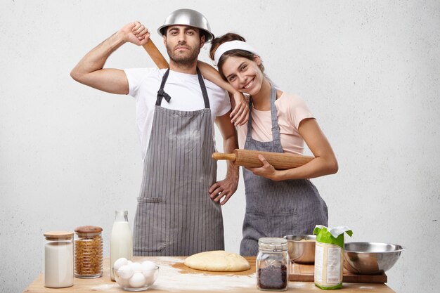 Smiling female model in apron leans at husband`s shoulder, recieves help and support from him