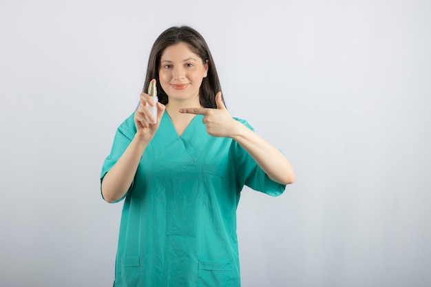 흰색에 스프레이 병을 보여주는 웃는 여성 간호사.