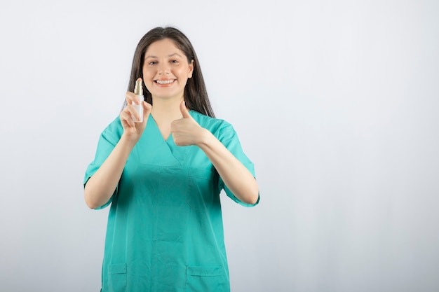 Smiling female nurse showing spray bottle on white. 