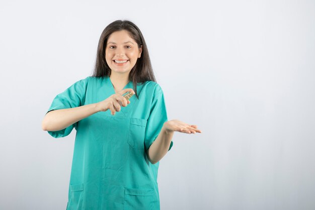 Smiling female nurse spraying her hand on white. 