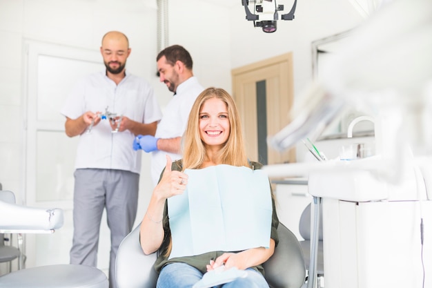 2人の男性の歯科医の前にオスのサインを身に着けている女性患者を笑って