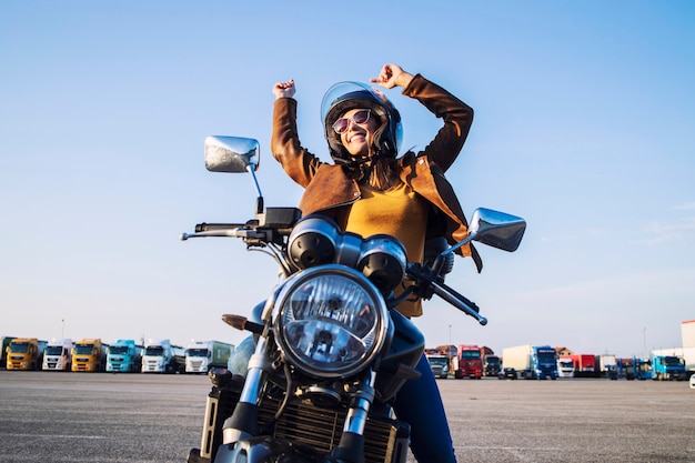 Smiling female rider sitting on her motorcycle with arms high showing happiness