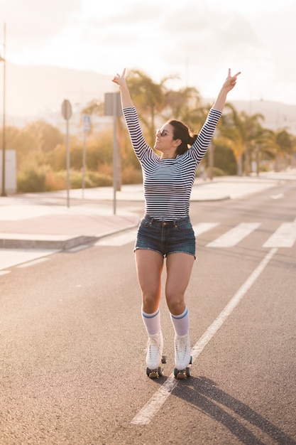 도로에 평화 제스처를 만드는 롤러 스케이트를 입고 웃는 여성 스케이팅