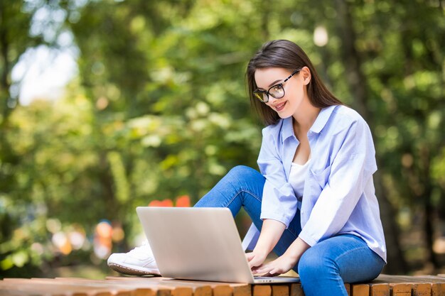 야외에서 노트북으로 벤치에 앉아 웃는 여자 학생