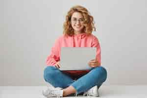 Free photo smiling female student writing essay, sitting with laptop on floor