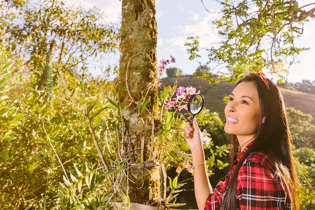 Smiling female tourist holding magnifying glass in front of flowers