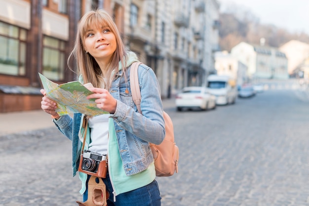 マップと都会の背景に立っている笑顔の女性旅行者