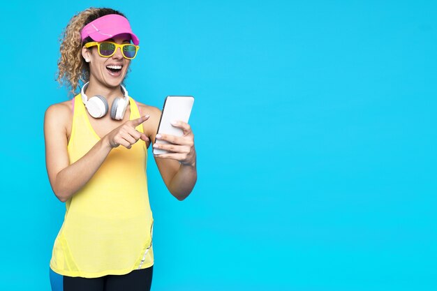 Smiling female with blonde curly hair holding a phone against a blue background