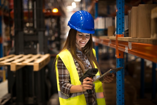 Smiling female worker holding tablet and bar code scanner checking inventory in distribution warehouse