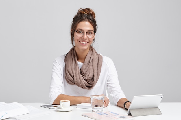 Smiling female writer creates new poem, types on tablet, has inspiration, drinks cappucino