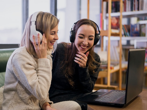Smiling females wearing headphones looking at laptop