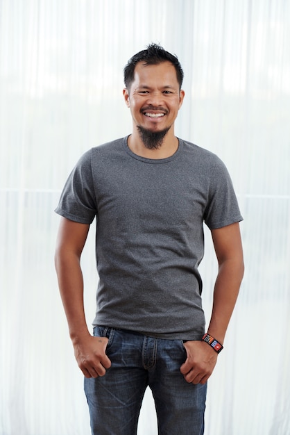 Smiling Filipino man standing with thumbs in pockets in front of brightly lit window