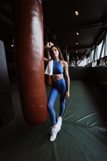 Smiling fit girl holding towel and taking rest in gym near punching bag