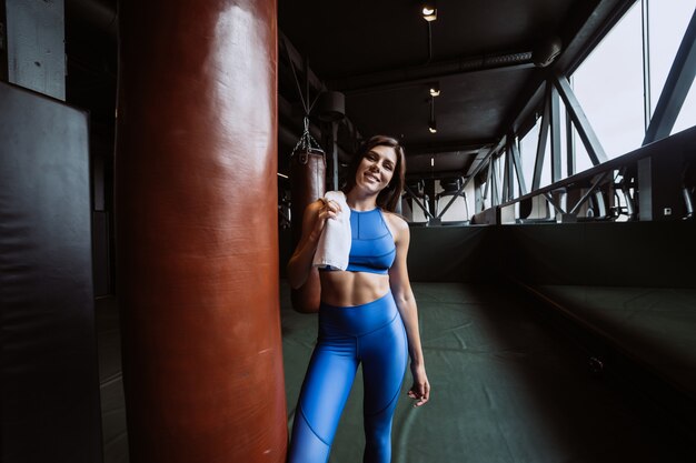 Smiling fit girl holding towel and taking rest in gym near punching bag