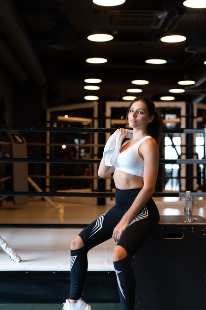 Smiling fit girl holding towel and taking rest in gym.