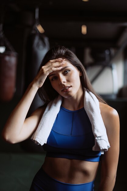 Smiling fit girl holding towel and taking rest in gym.