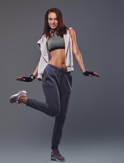 Smiling fitness brunette female in a gray sportswear posing in a studio. Isolated on a gray background.