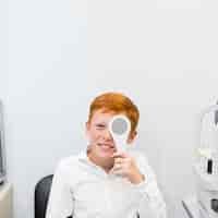 Free photo smiling freckle boy holding occluder in front of his eye in ophthalmological clinic