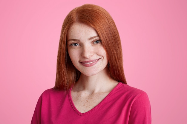 Smiling freckled female with straight luxurious red hair, being glad to receive good job proposal