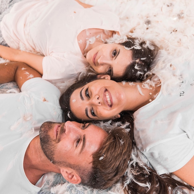 Smiling friends lying on bed with white feathers