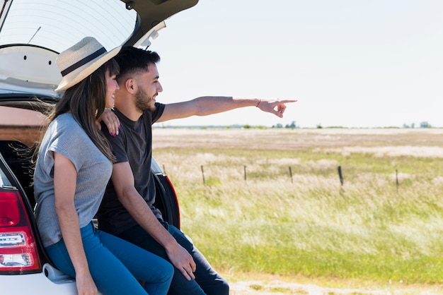 Smiling friends sitting on a car pointing at something