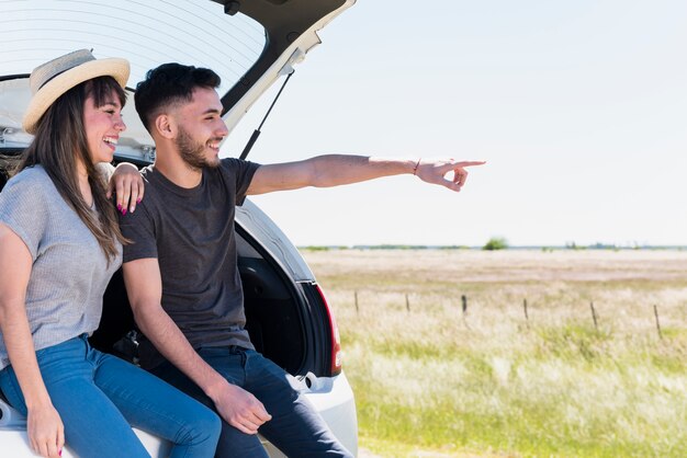 Smiling friends sitting on a car pointing at something