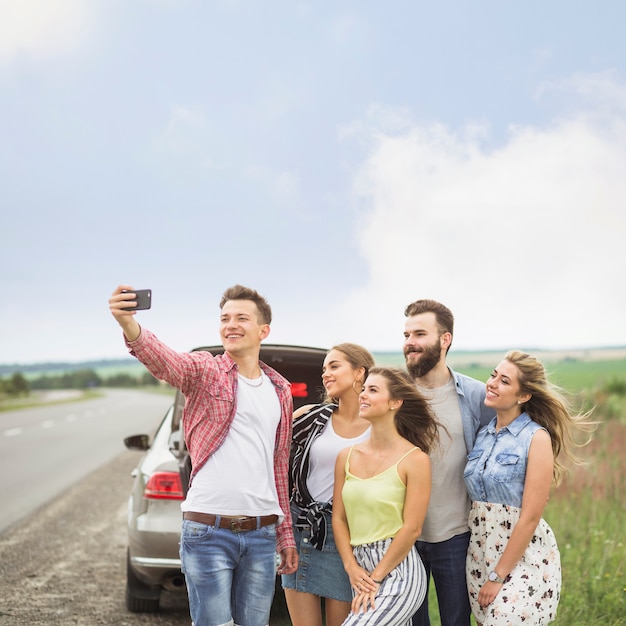 Foto gratuita amici sorridenti che stanno vicino all'automobile parcheggiata che prende autoritratto