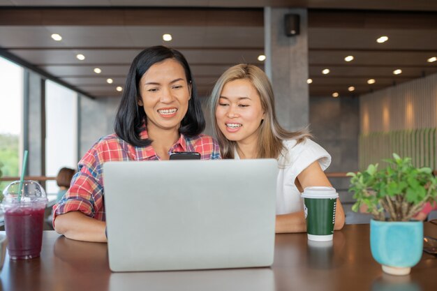 Smiling friends with hot drink using laptop in cafe