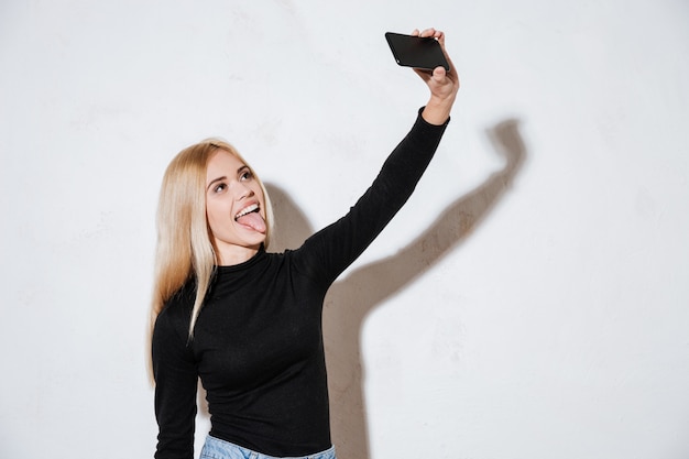 Smiling funny woman showing tongue while taking selfie