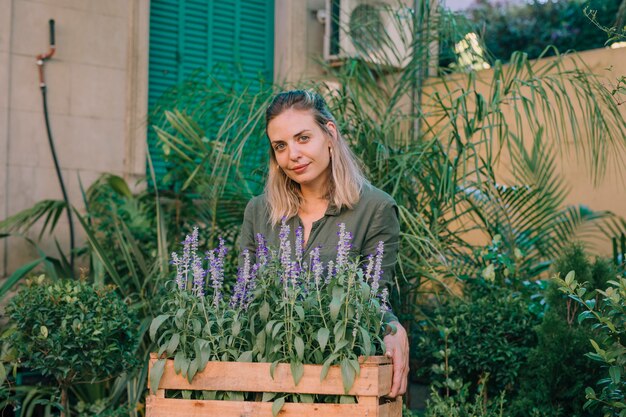 Smiling gardener carrying lavender flower pots in crate at plant nursery