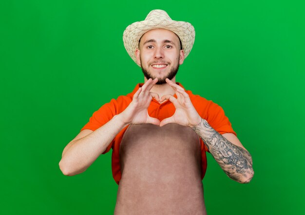 Smiling gardener man wearing gardening hat gestures heart hand sign