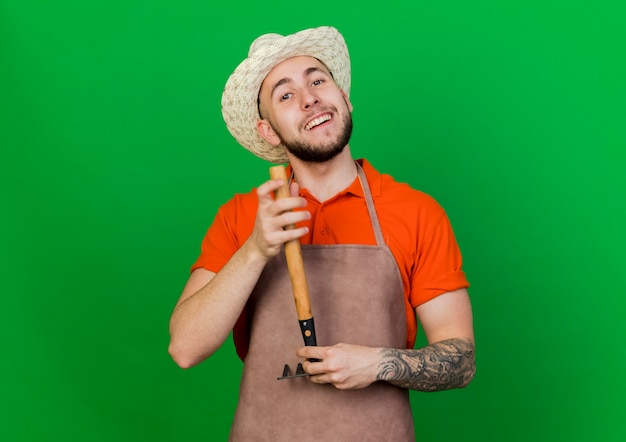 Smiling gardener man wearing gardening hat holds rake upside down 