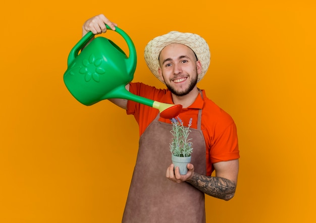 Smiling gardener man wearing gardening hat holds watering can pretending to water plant in flowerpot 