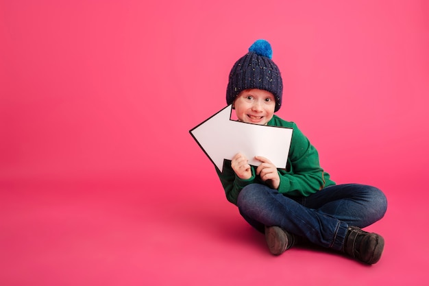 Smiling ginger boy holding arrow left and looking camera