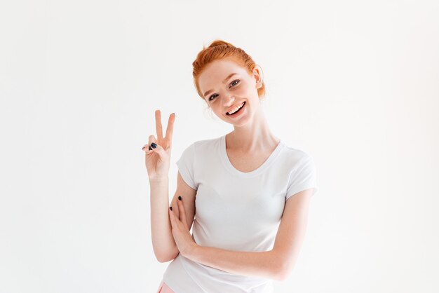 Smiling ginger woman in t-shirt showing peace gesture and looking