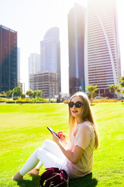 Smiling girl in black sunglasses sits on bright green lawn in Dubai