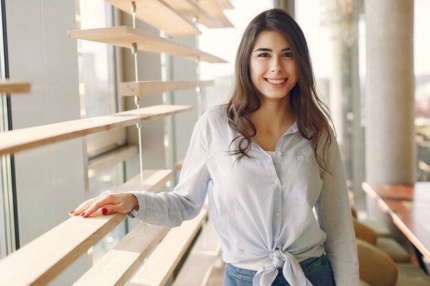 Smiling girl in a blue shirt standing near window and posing