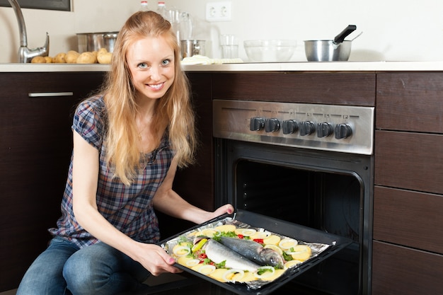 Бесплатное фото Улыбающаяся девушка приготовления сырой рыбы в духовке