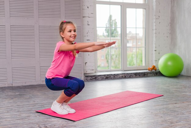 Smiling girl crouching and exercising on pink mat