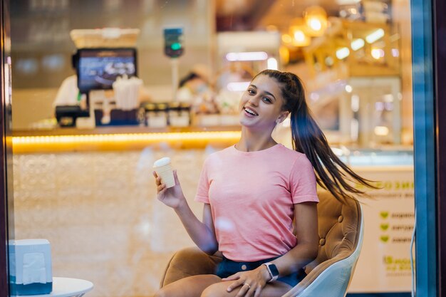 Smiling girl eating an ice-cream in a waffle cup in a cafe