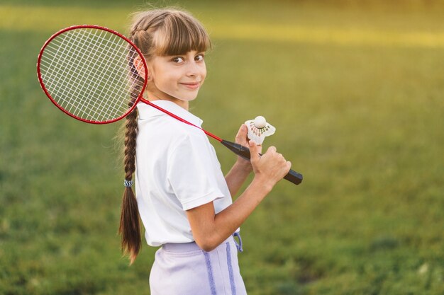 Smiling girl holding badminton over her shoulder and shuttlecock