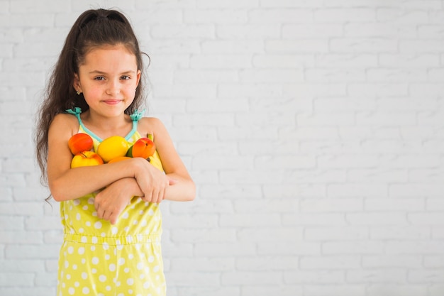 Smiling girl holding colorful fruits in her two arms