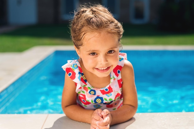 Foto gratuita ragazza sorridente che si aggrappa al lato della piscina e guarda nell'obiettivo